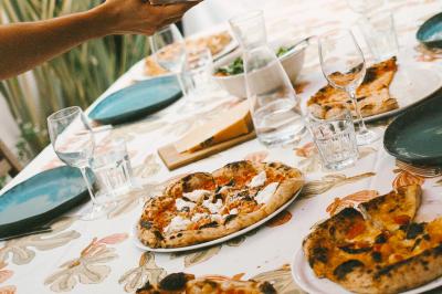 Miniature Traiteur Paris (Paris) - Pizzaiolo Tsogani #8 Un homme retire une pizza du four à l'aide d'une pelle, accompagné d'une femme souriante dans une cuisine moderne.
