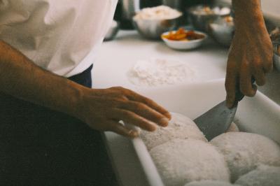 Miniature Traiteur Paris (Paris) - Pizzaiolo Tsogani #15 Un homme retire une pizza du four à l'aide d'une pelle, accompagné d'une femme souriante dans une cuisine moderne.