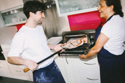 Miniature Traiteur Paris (Paris) - Pizzaiolo Tsogani #20 Un homme retire une pizza du four à l'aide d'une pelle, accompagné d'une femme souriante dans une cuisine moderne.