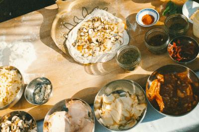 Miniature Traiteur Paris (Paris) - Pizzaiolo Tsogani #5 Un homme retire une pizza du four à l'aide d'une pelle, accompagné d'une femme souriante dans une cuisine moderne.