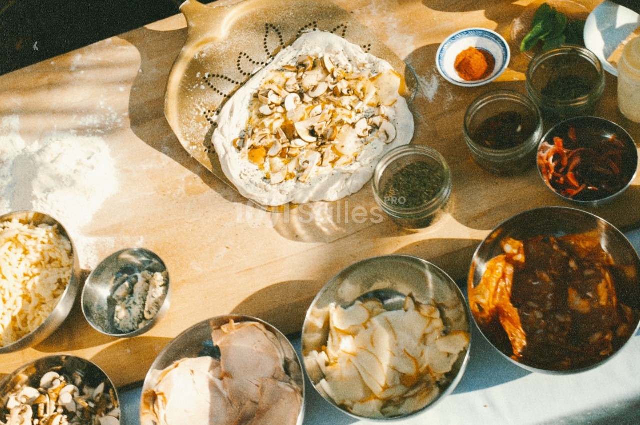 Ingrédients variés et pâte à pizza garnie de champignons disposés sur une table en bois.