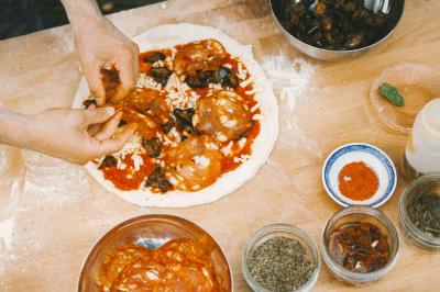 Miniature Traiteur Paris (Paris) - Pizzaiolo Tsogani #8 Un homme retire une pizza du four à l'aide d'une pelle, accompagné d'une femme souriante dans une cuisine moderne.