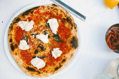 Miniature Traiteur Paris (Paris) - Pizzaiolo Tsogani #4 Un homme retire une pizza du four à l'aide d'une pelle, accompagné d'une femme souriante dans une cuisine moderne.