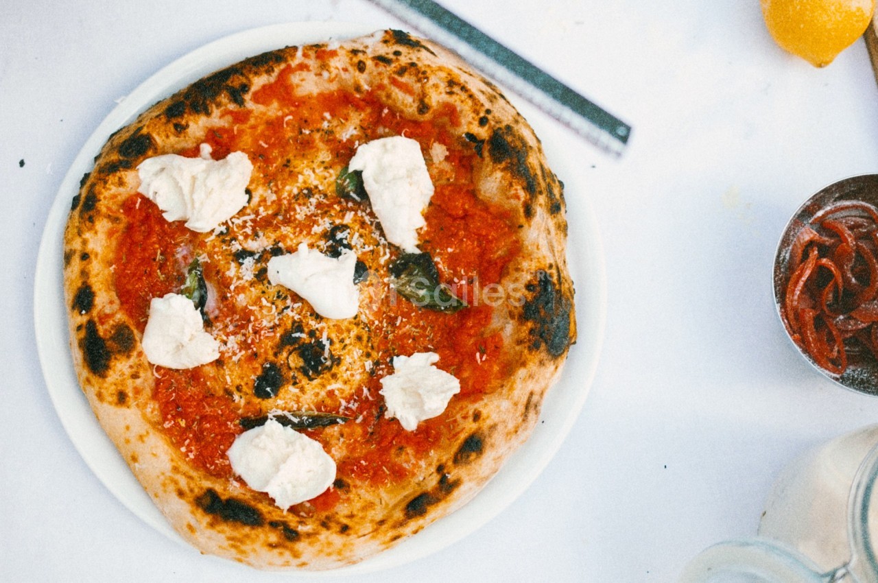 Pizza napolitaine garnie de sauce tomate, mozzarella, basilic et fromage râpé, servie sur une assiette blanche.