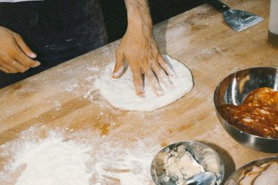 Miniature Traiteur Paris (Paris) - Pizzaiolo Tsogani #13 Un homme retire une pizza du four à l'aide d'une pelle, accompagné d'une femme souriante dans une cuisine moderne.