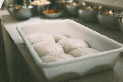 Miniature Traiteur Paris (Paris) - Pizzaiolo Tsogani #15 Un homme retire une pizza du four à l'aide d'une pelle, accompagné d'une femme souriante dans une cuisine moderne.