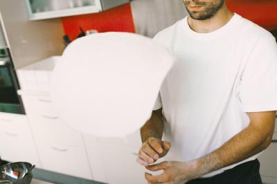 Miniature Traiteur Paris (Paris) - Pizzaiolo Tsogani #17 Un homme retire une pizza du four à l'aide d'une pelle, accompagné d'une femme souriante dans une cuisine moderne.