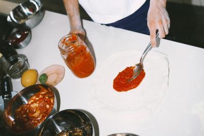 Miniature Traiteur Paris (Paris) - Pizzaiolo Tsogani #18 Un homme retire une pizza du four à l'aide d'une pelle, accompagné d'une femme souriante dans une cuisine moderne.
