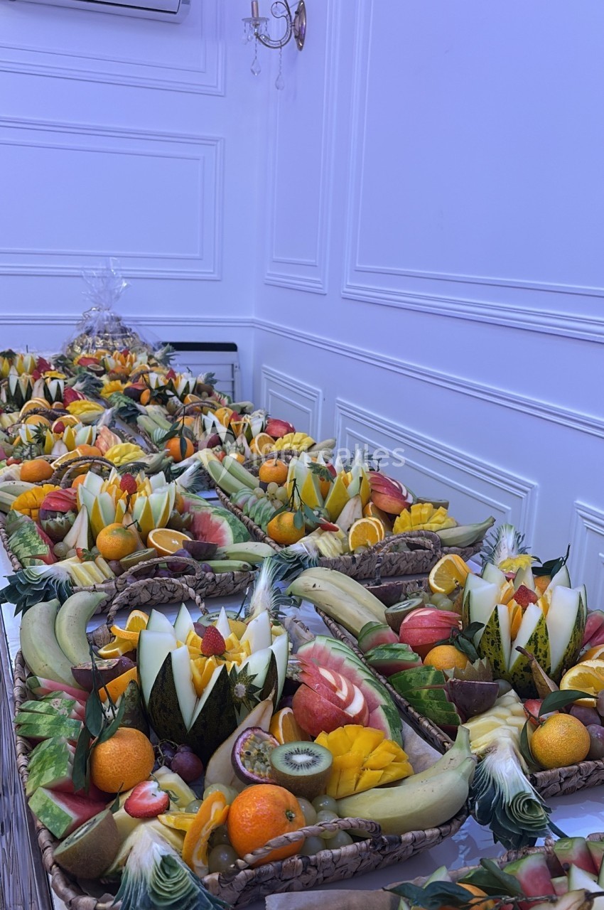 Plateau de fruits variés joliment découpés et disposés sur une longue table dans une salle blanche.