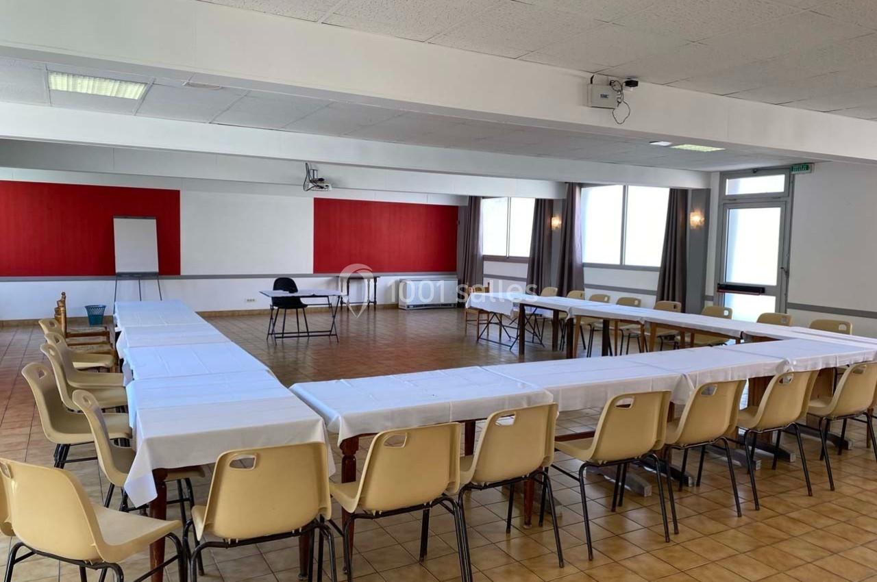 Salle de réunion lumineuse avec tables disposées en U, chaises beige, tableau blanc et projecteur au plafond.