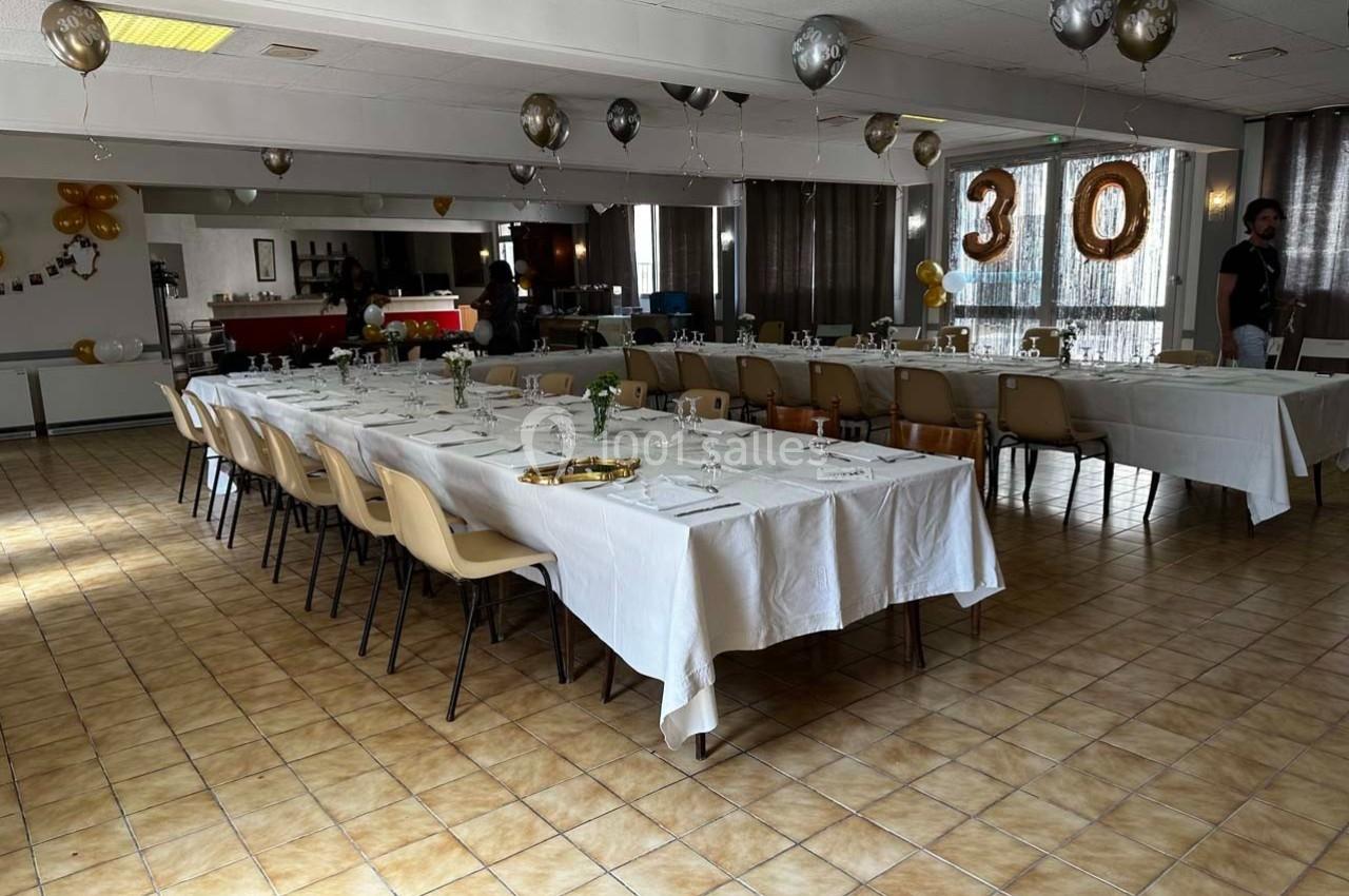 Salle décorée pour un 30e anniversaire avec tables dressées, ballons et guirlandes dans un espace lumineux.