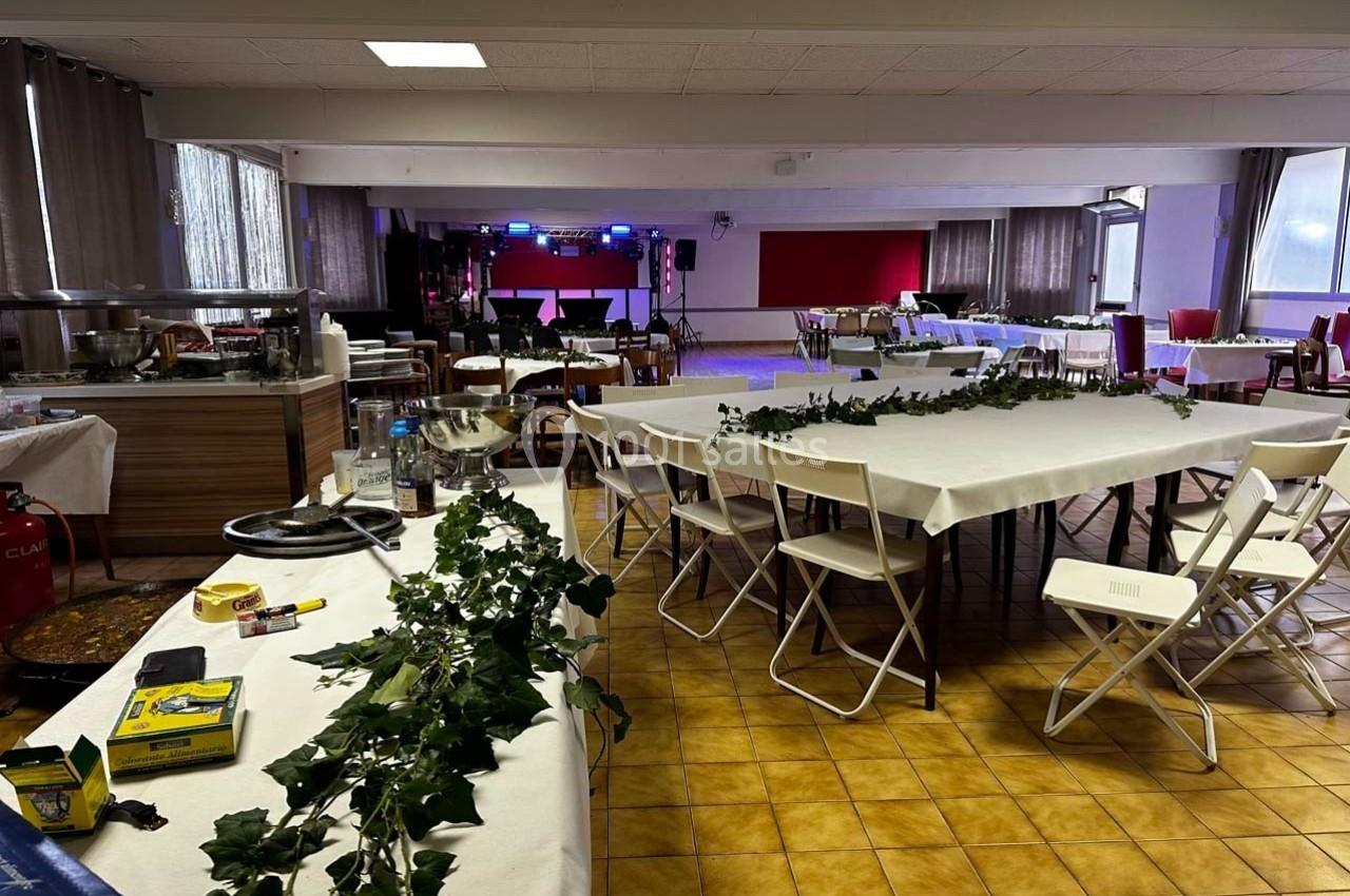 Salle de réception en préparation avec des tables décorées de feuillage et une scène équipée de lumières au fond.