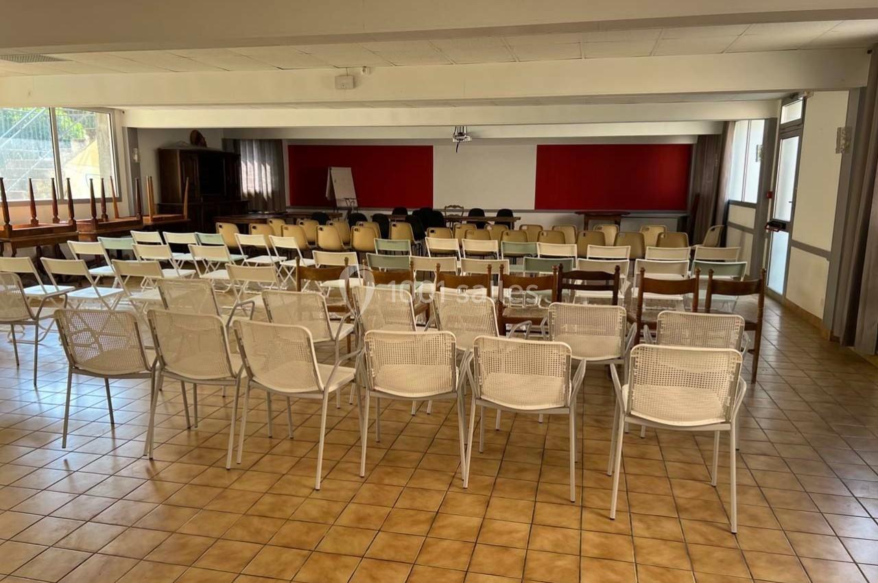 Salle de réunion avec des rangées de chaises blanches et beiges, face à un tableau blanc et un mur rouge.