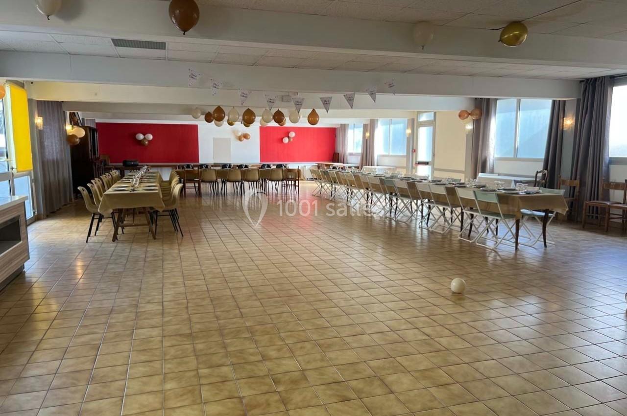 Salle de réception lumineuse avec tables alignées et décorations suspendues, prête pour un événement.