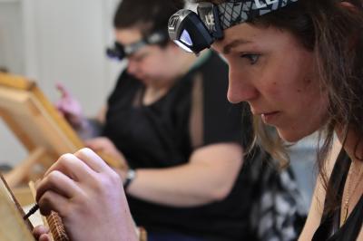 Deux femmes concentrées réalisent un travail minutieux à la main, éclairées par des lampes frontales.