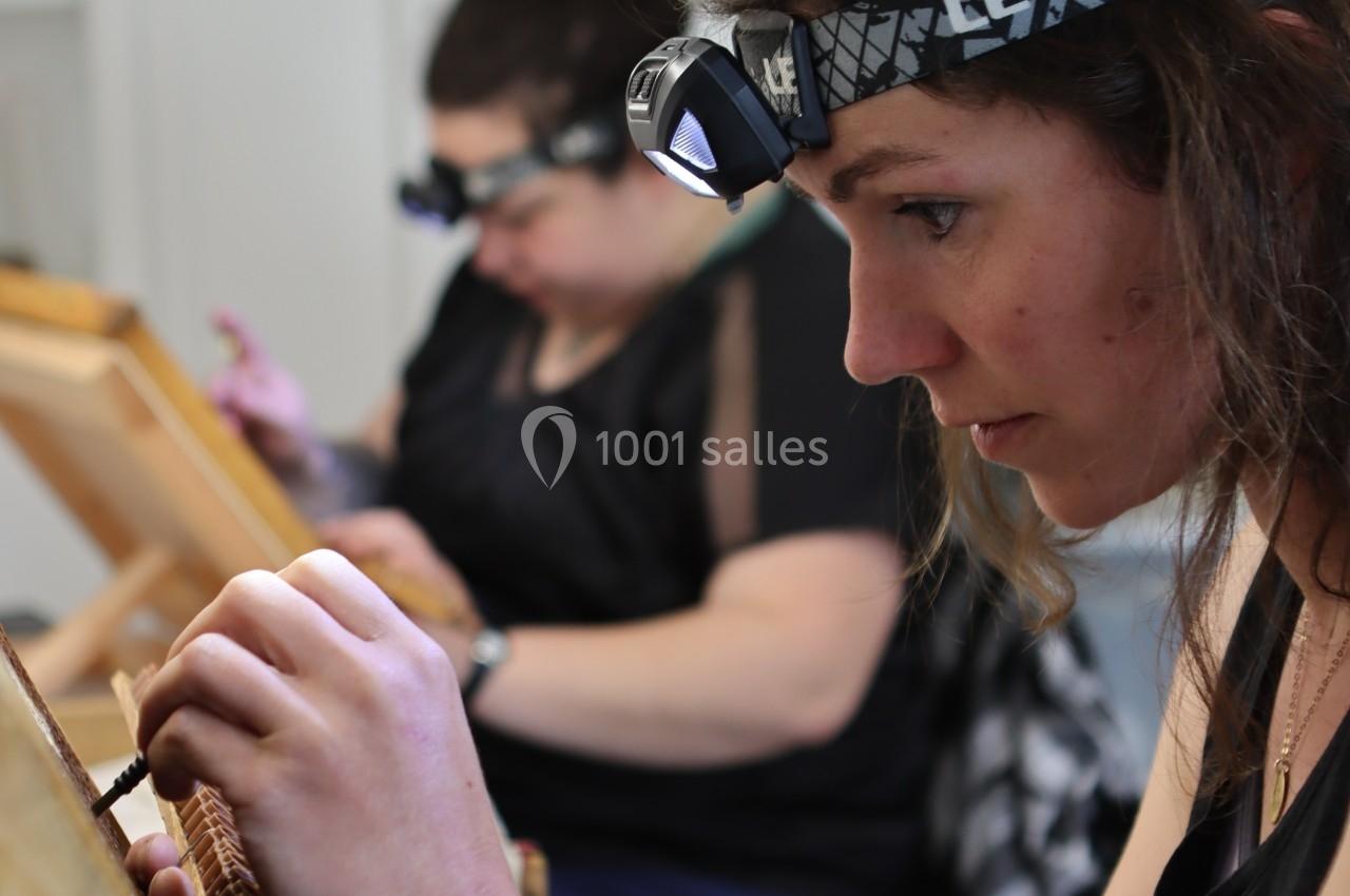 Deux femmes concentrées réalisent un travail minutieux à la main, éclairées par des lampes frontales.
