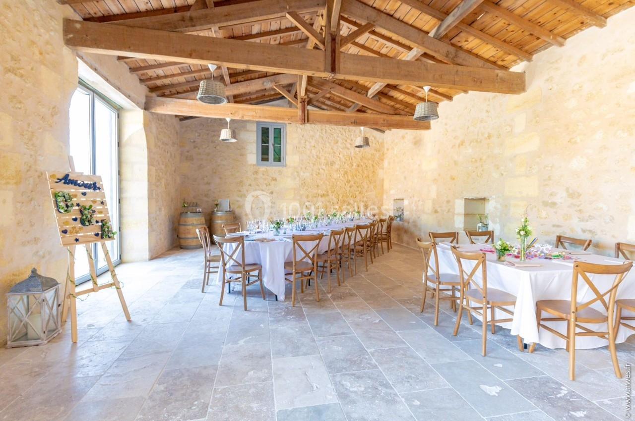 Salle en pierre lumineuse avec tables rondes et rectangulaires dressées, décorée pour un événement.