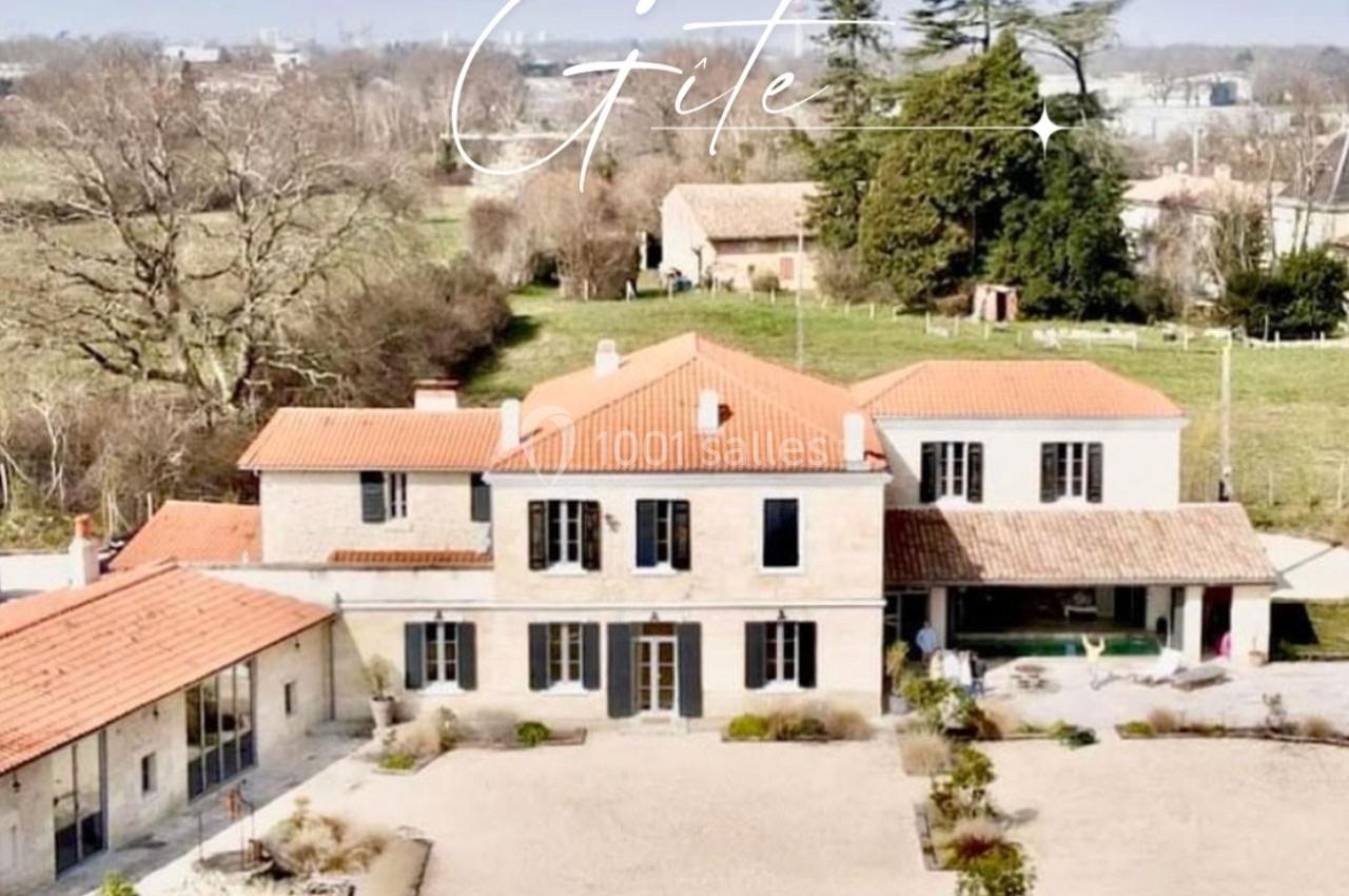 Vue aérienne d'un grand gîte en pierre avec toit en tuiles, entouré de jardins et d'arbres dans un cadre rural.