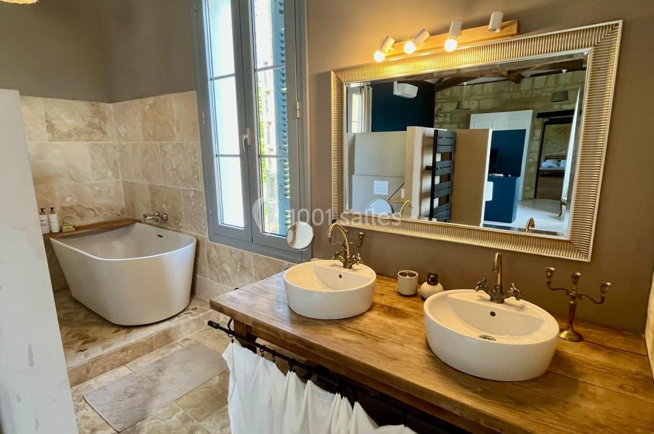 Salle de bain avec baignoire îlot, double vasque sur meuble en bois et miroir encadré, éclairée par une fenêtre.