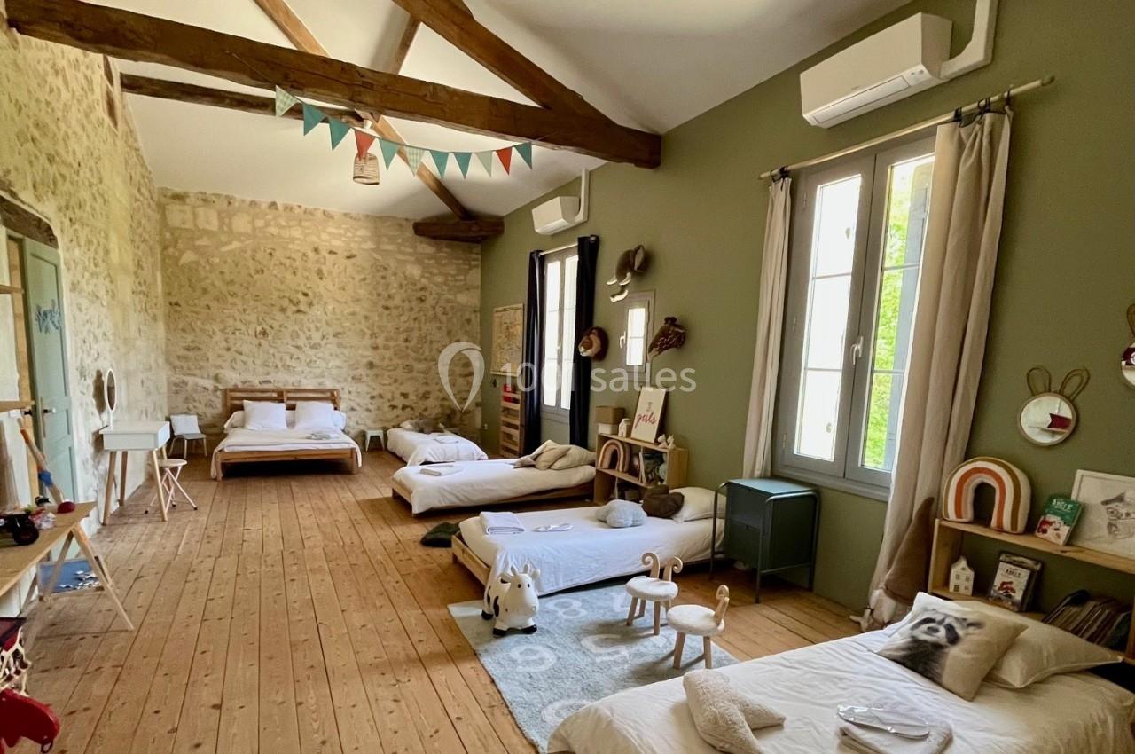 Chambre spacieuse avec lits pour enfants, murs en pierre, poutres apparentes et décoration chaleureuse.