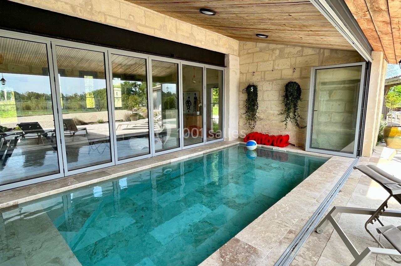 Piscine intérieure avec margelles en pierre, entourée de baies vitrées et d'un plafond en bois.