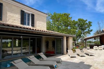 Miniature Location salle Tresses (Gironde) - Domaine de la Rose Blanche #16 Façade d'une maison en pierre avec terrasse ensoleillée, chaises longues et pots de fleurs sur un sol pavé clair.