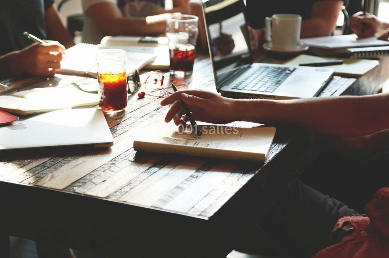 Personnes travaillant autour d'une table en bois avec ordinateurs, cahiers et boissons.