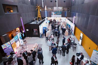 Des personnes échangent dans un espace d'exposition intérieur avec des stands et une structure métallique visible en arrière…