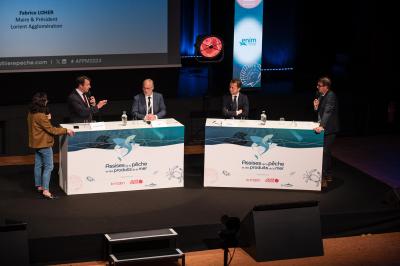 Des personnes échangent dans un espace d'exposition intérieur avec des stands et une structure métallique visible en arrière…