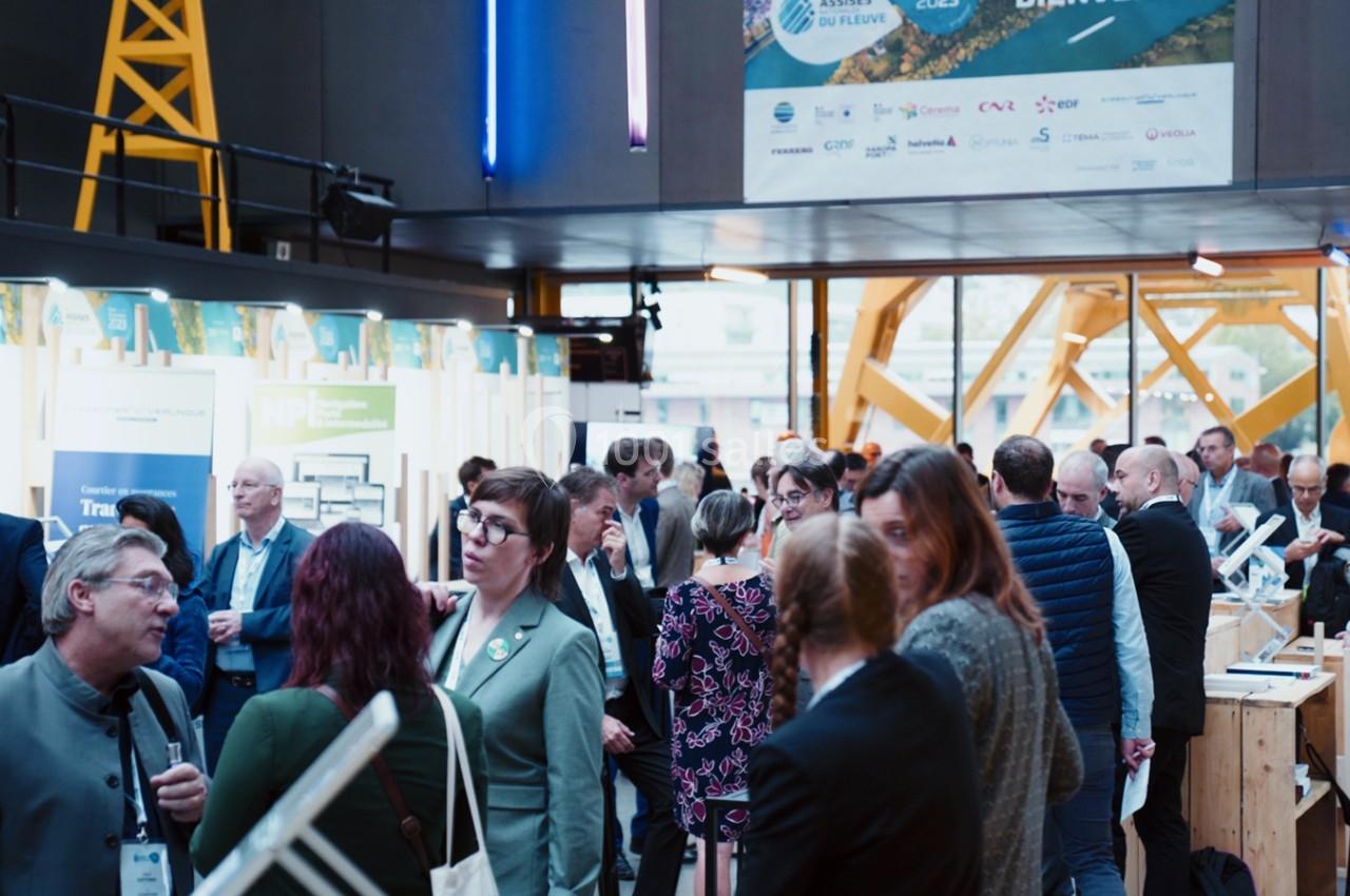 Des personnes échangent dans un espace d'exposition intérieur avec des stands et une structure métallique visible en arrière…