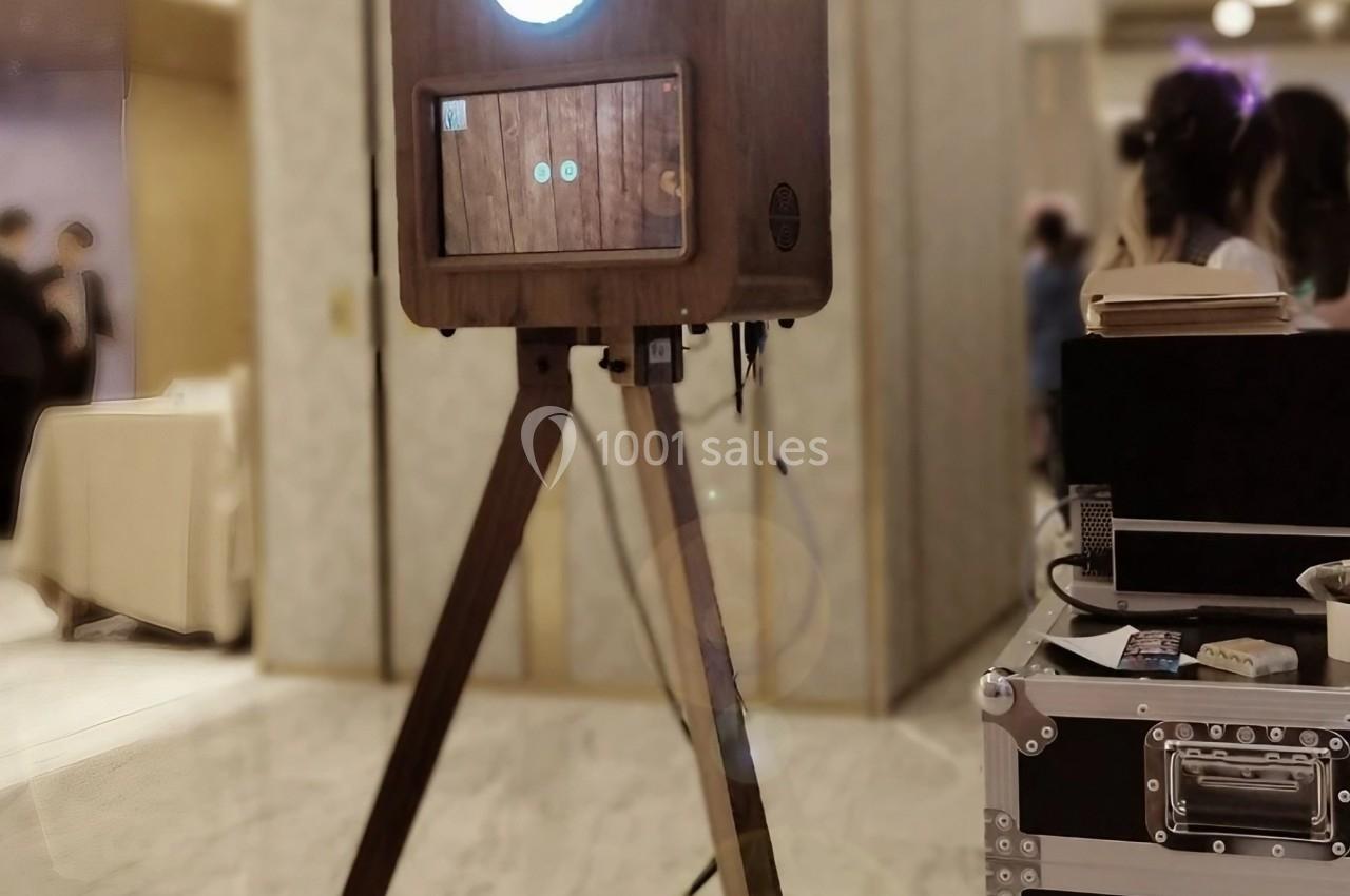 Borne photo vintage en bois sur trépied, installée dans un espace intérieur lumineux avec des personnes en arrière-plan.