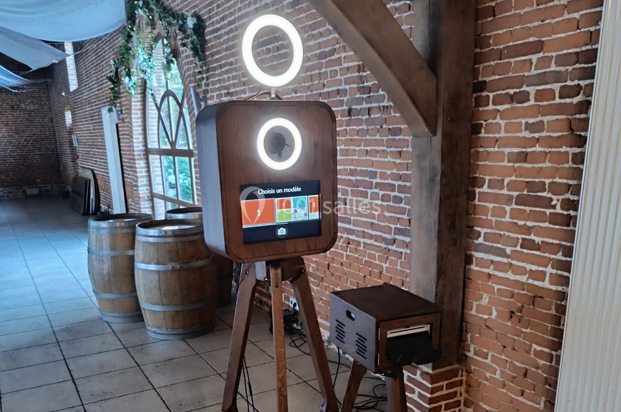 Borne photo en bois avec écran tactile et anneaux lumineux, installée dans une salle aux murs de briques.
