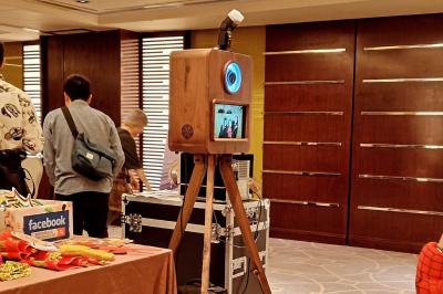 Borne photo en bois sur trépied avec un anneau lumineux allumé, installée dans un espace intérieur.