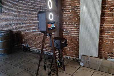 Borne photo en bois sur trépied avec un anneau lumineux allumé, installée dans un espace intérieur.