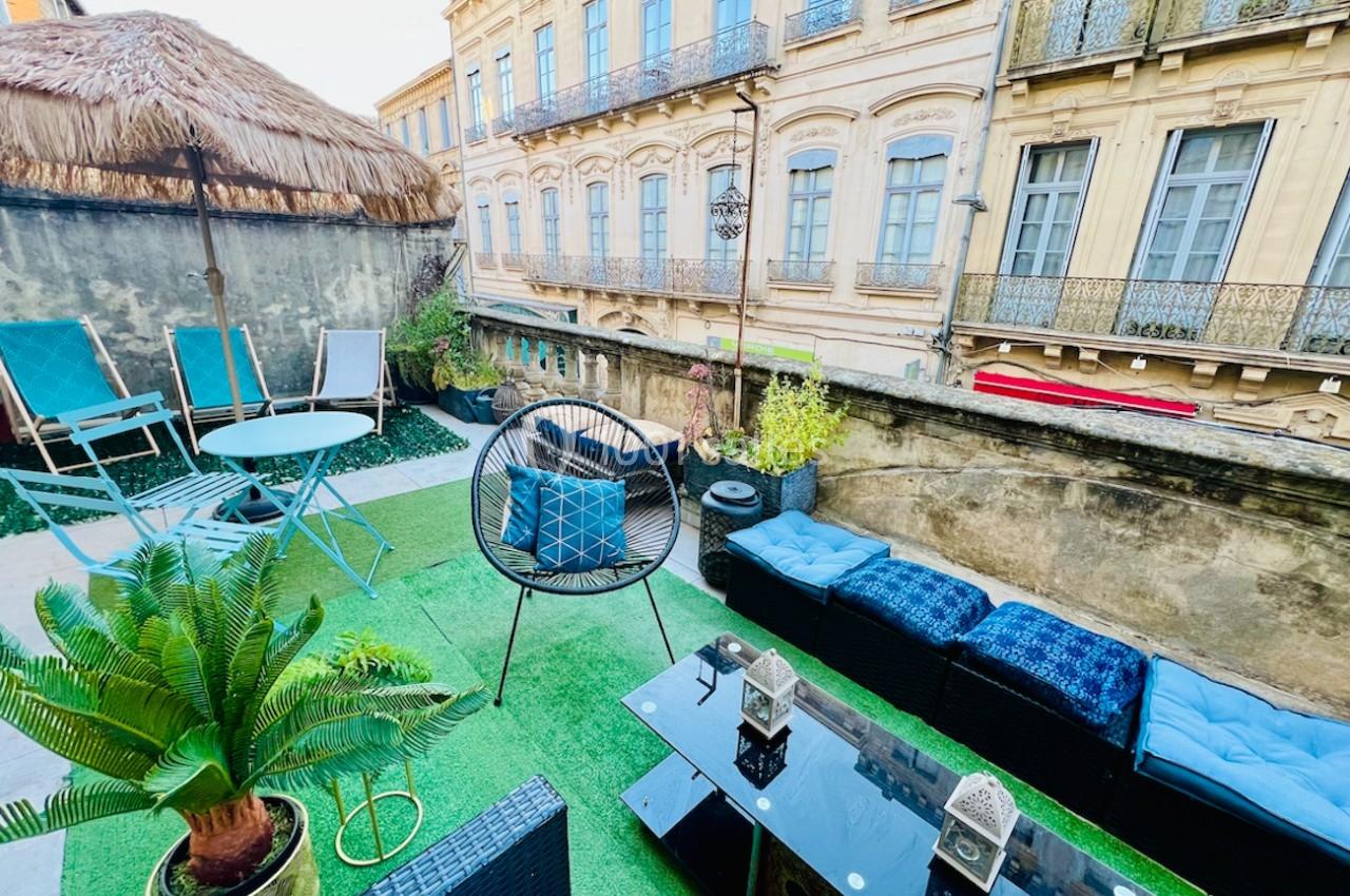 Terrasse aménagée avec mobilier de jardin, pelouse artificielle, plantes et vue sur des façades anciennes en pierre.
