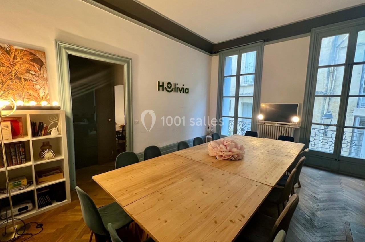 Salle de réunion lumineuse avec une grande table en bois, des chaises vertes et des fenêtres donnant sur l'extérieur.