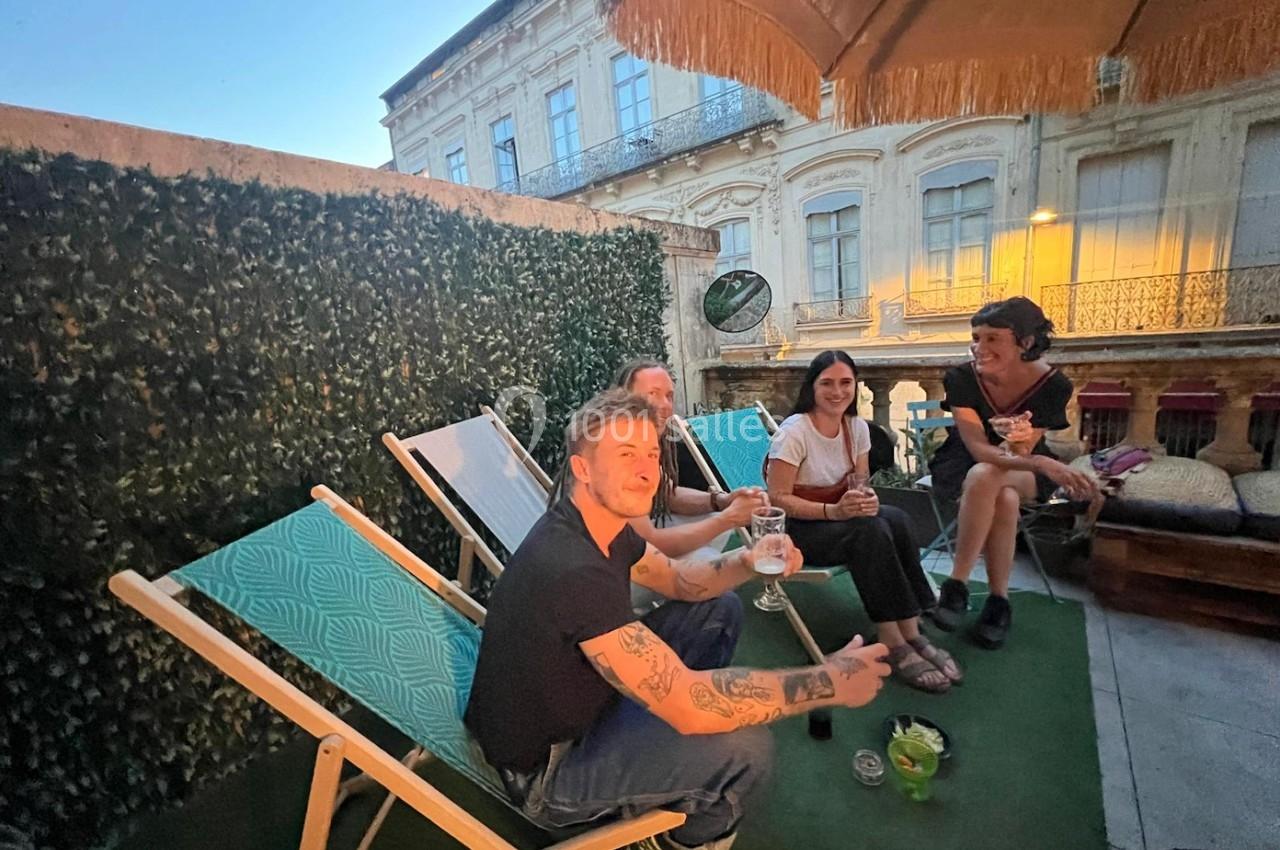 Des personnes assises sur une terrasse en soirée, discutant et partageant des boissons sous un parasol.
