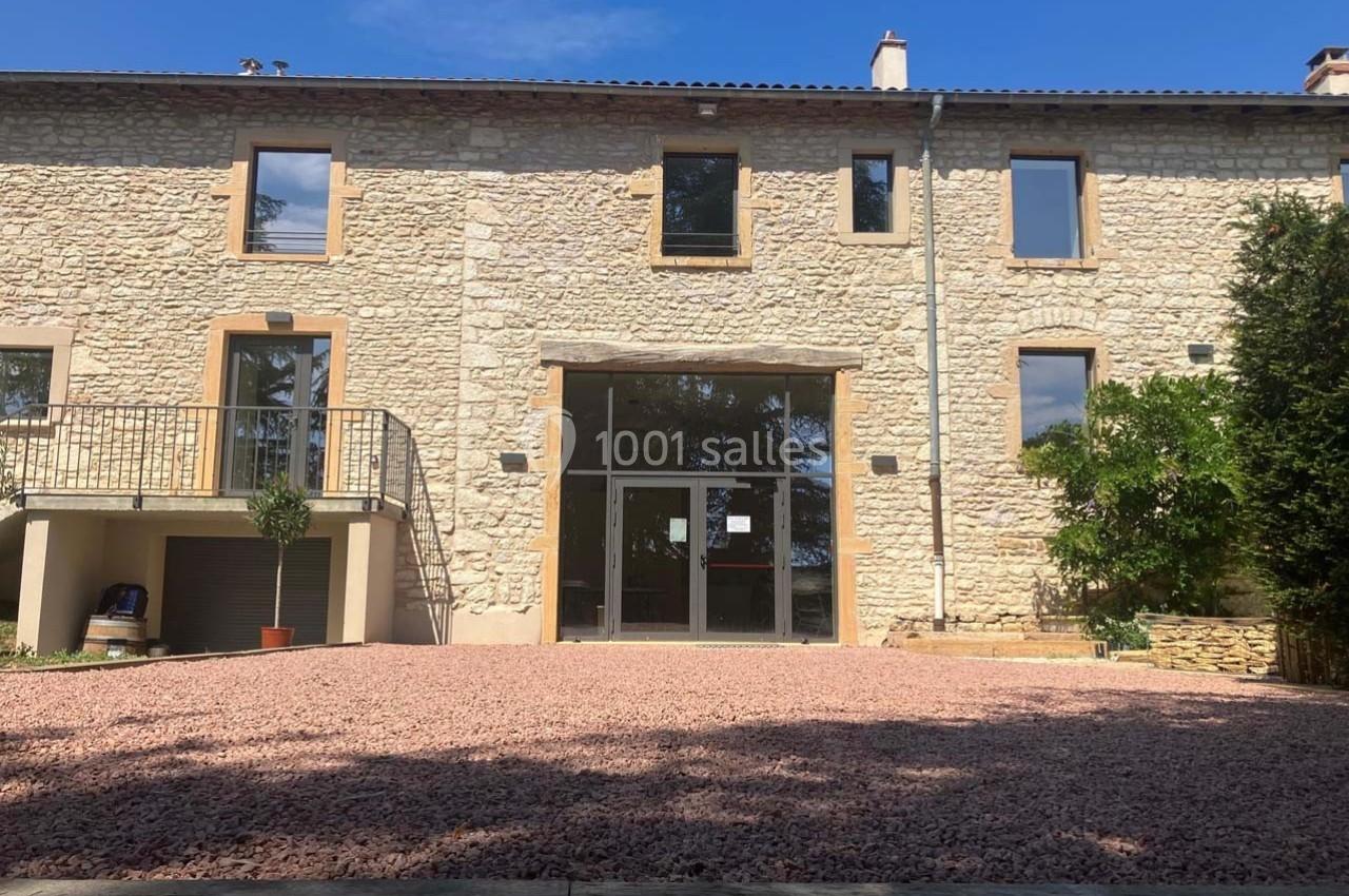 Façade d'une maison en pierre rénovée avec de grandes baies vitrées, entourée d'une cour en gravier.