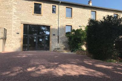 Miniature Location salle Pommiers (Rhône) - Domaine Nicolas Rebut #3 Façade d'un bâtiment en pierre avec de grandes fenêtres, une entrée vitrée et une cour en gravier sous un ciel bleu.