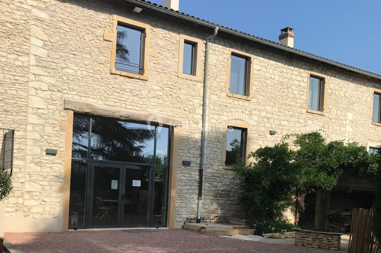 Façade en pierre d'un bâtiment avec de grandes fenêtres, une entrée vitrée et un espace extérieur gravillonné.