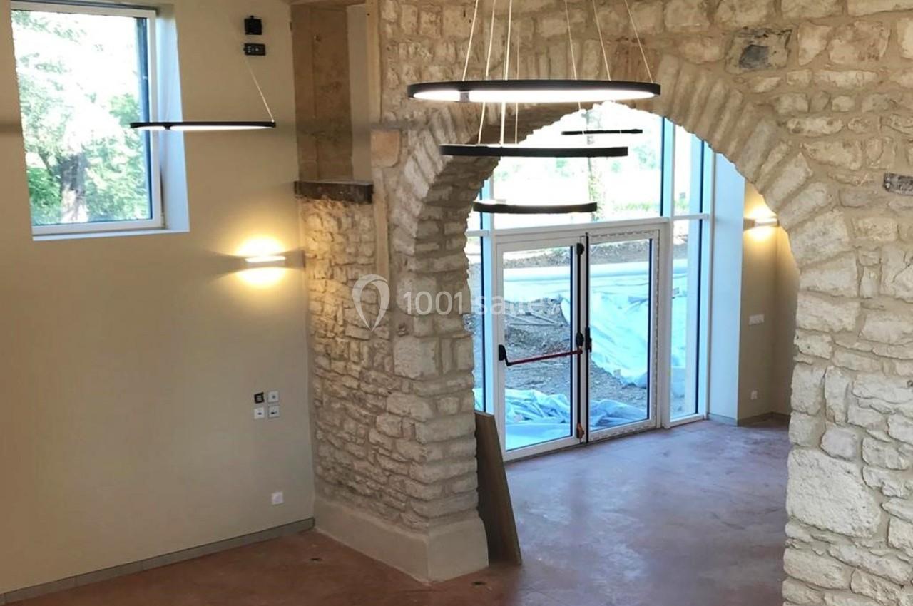 Intérieur d'une pièce rénovée avec murs en pierre, grandes fenêtres et luminaires suspendus modernes.