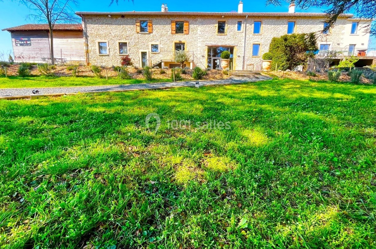 Façade d'une maison en pierre avec un grand jardin verdoyant sous un ciel bleu clair.