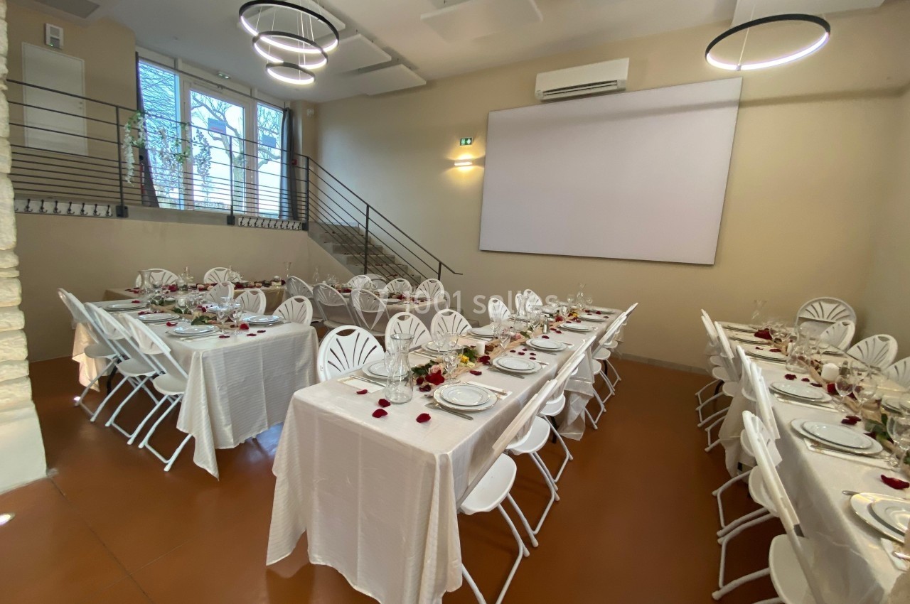 Salle de réception avec tables dressées, nappes blanches, chaises pliantes et décoration florale minimaliste.
