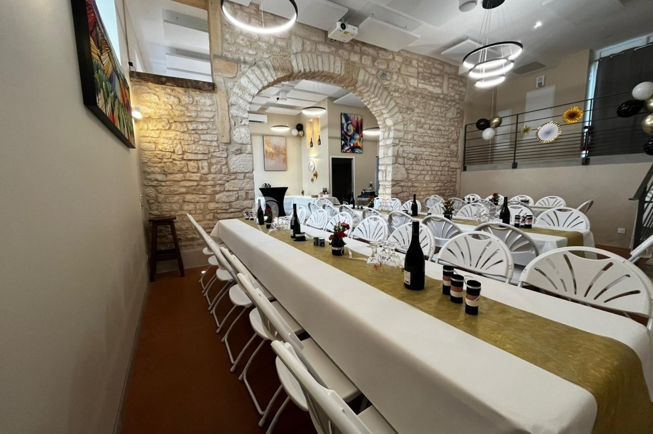 Salle de réception avec longues tables dressées, nappes blanches, décorations murales et pierres apparentes.