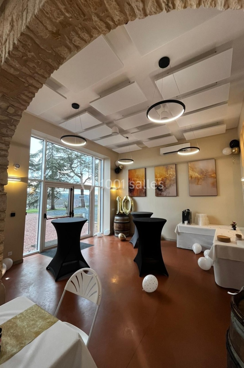 Salle décorée avec des tables hautes noires, des ballons et une vue sur l'extérieur à travers une grande baie vitrée.