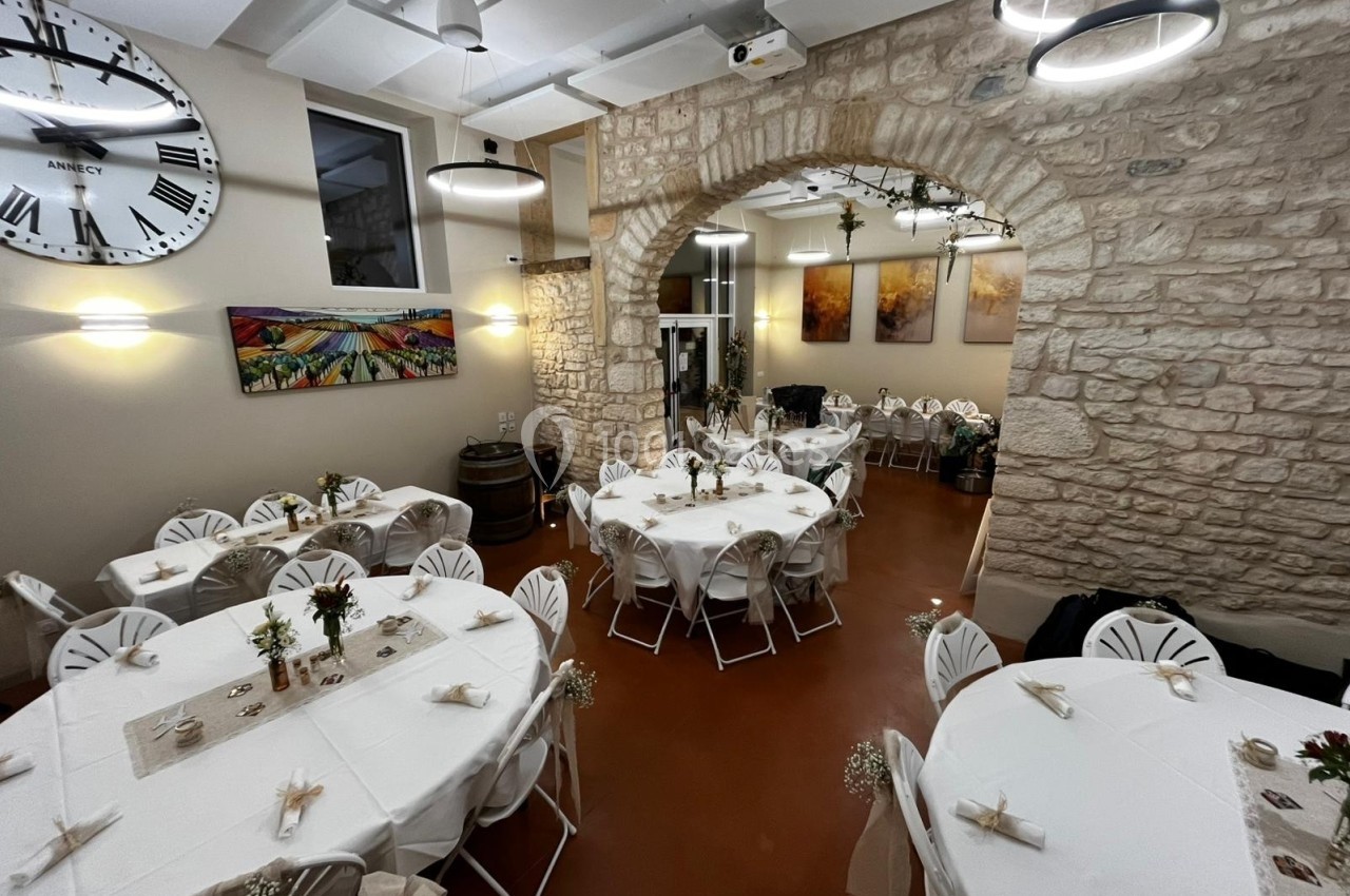 Salle de réception avec murs en pierre, tables rondes dressées et décorations florales sous un éclairage chaleureux.