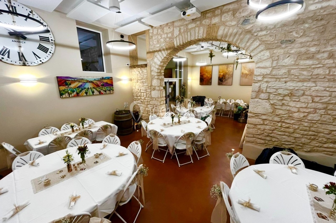 Salle de réception décorée avec des tables rondes dressées, murs en pierre apparente et éclairage chaleureux.