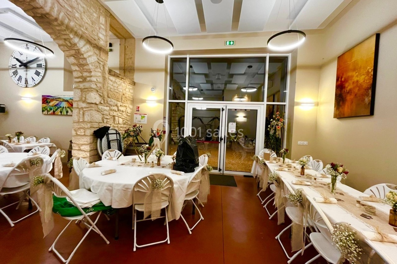 Salle de réception décorée avec des tables rondes, nappes blanches, chaises pliantes et arrangements floraux.