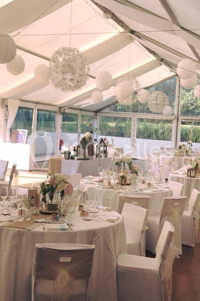 Salle de réception décorée avec des tables rondes, nappes blanches, fleurs et suspensions lumineuses.