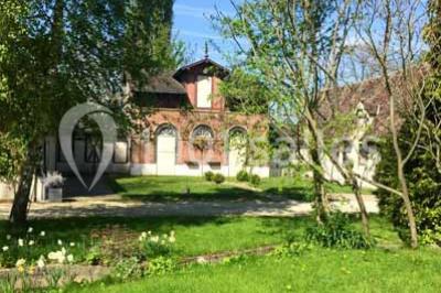 Glycine en fleurs grimpant sur une pergola, avec une maison en briques et des arbustes en arrière-plan.